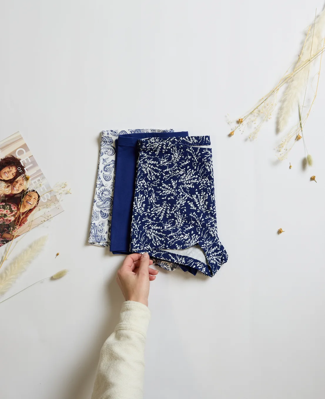 Blå mönstrade badshorts på vit bakgrund med torkade blommor